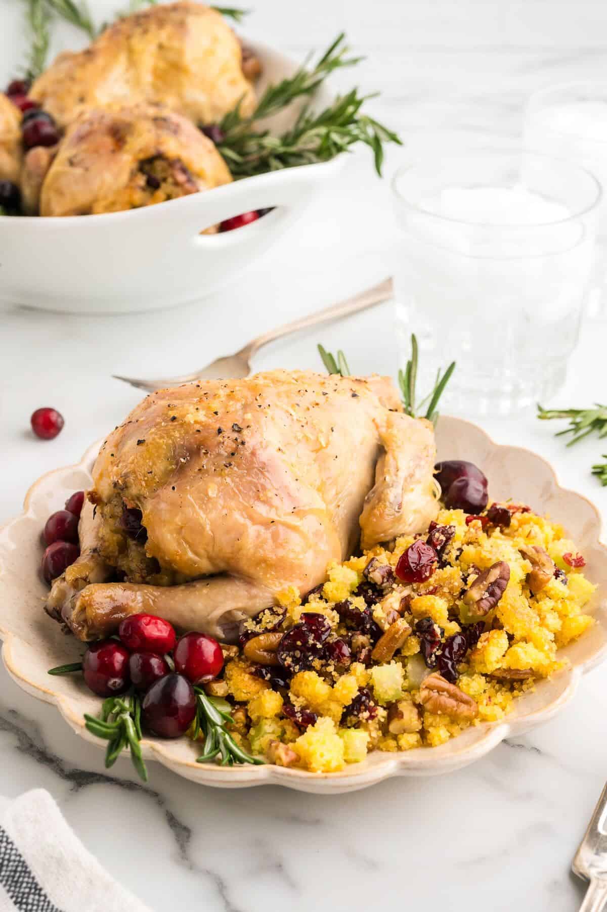 A stuffed cornish hen on a plate next to cornbread stuffing. 