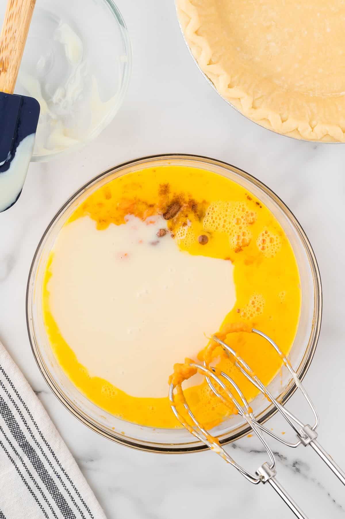 A clear glass bowl with eggs, condensed milk and mashed sweet potatoes. 