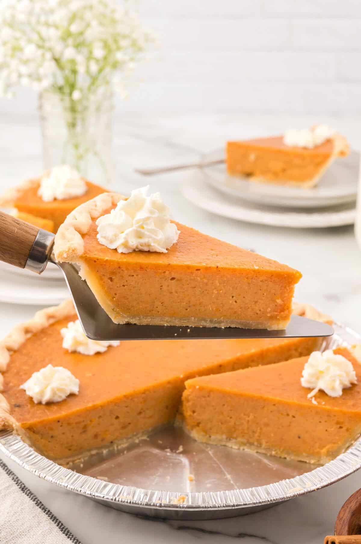 A slice of sweet potato pie topped with a dollop of whipped cream next to the rest of the pie. 