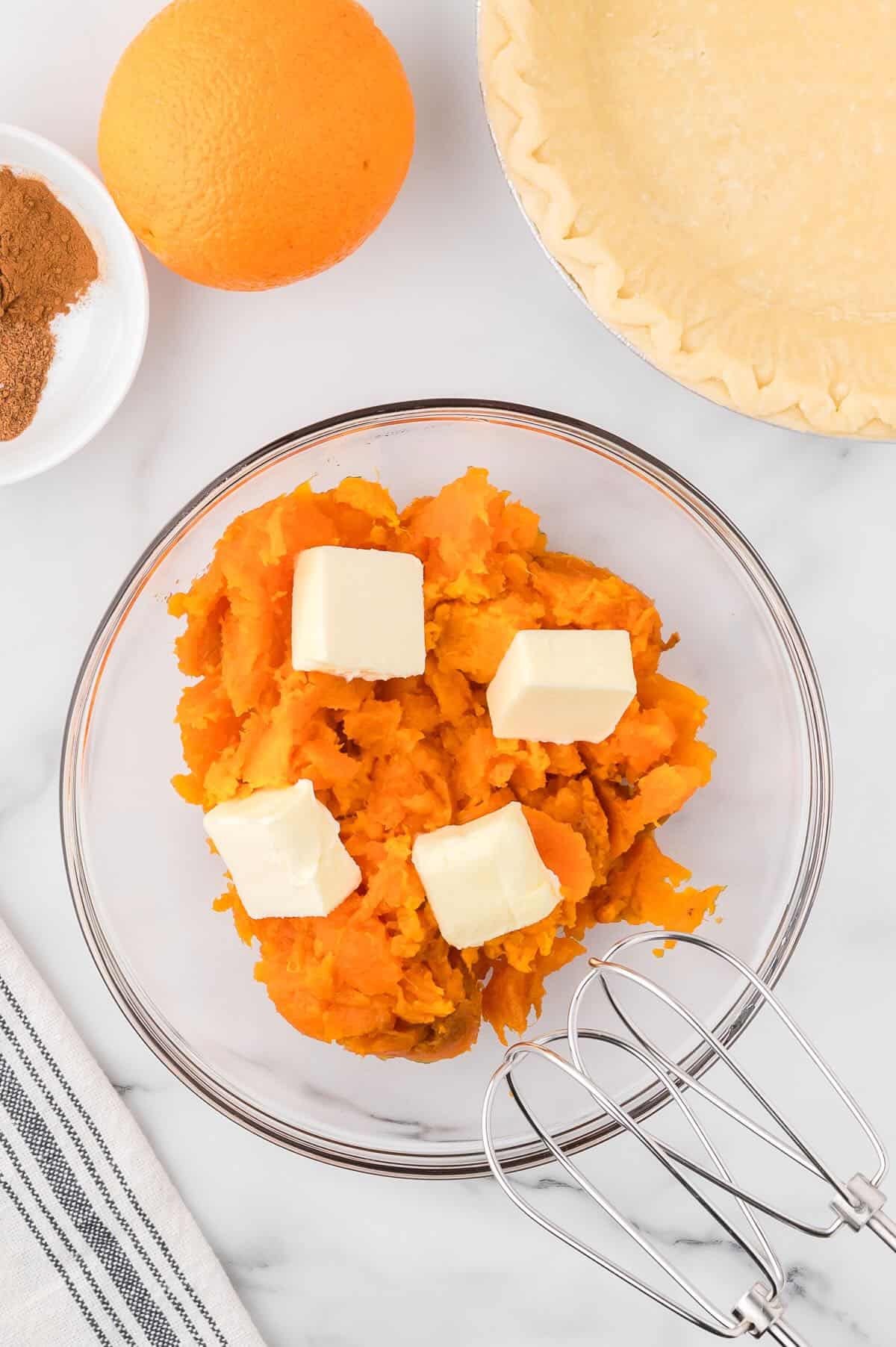 A clear glass bowl with cooked mashed sweet potato and butter. 