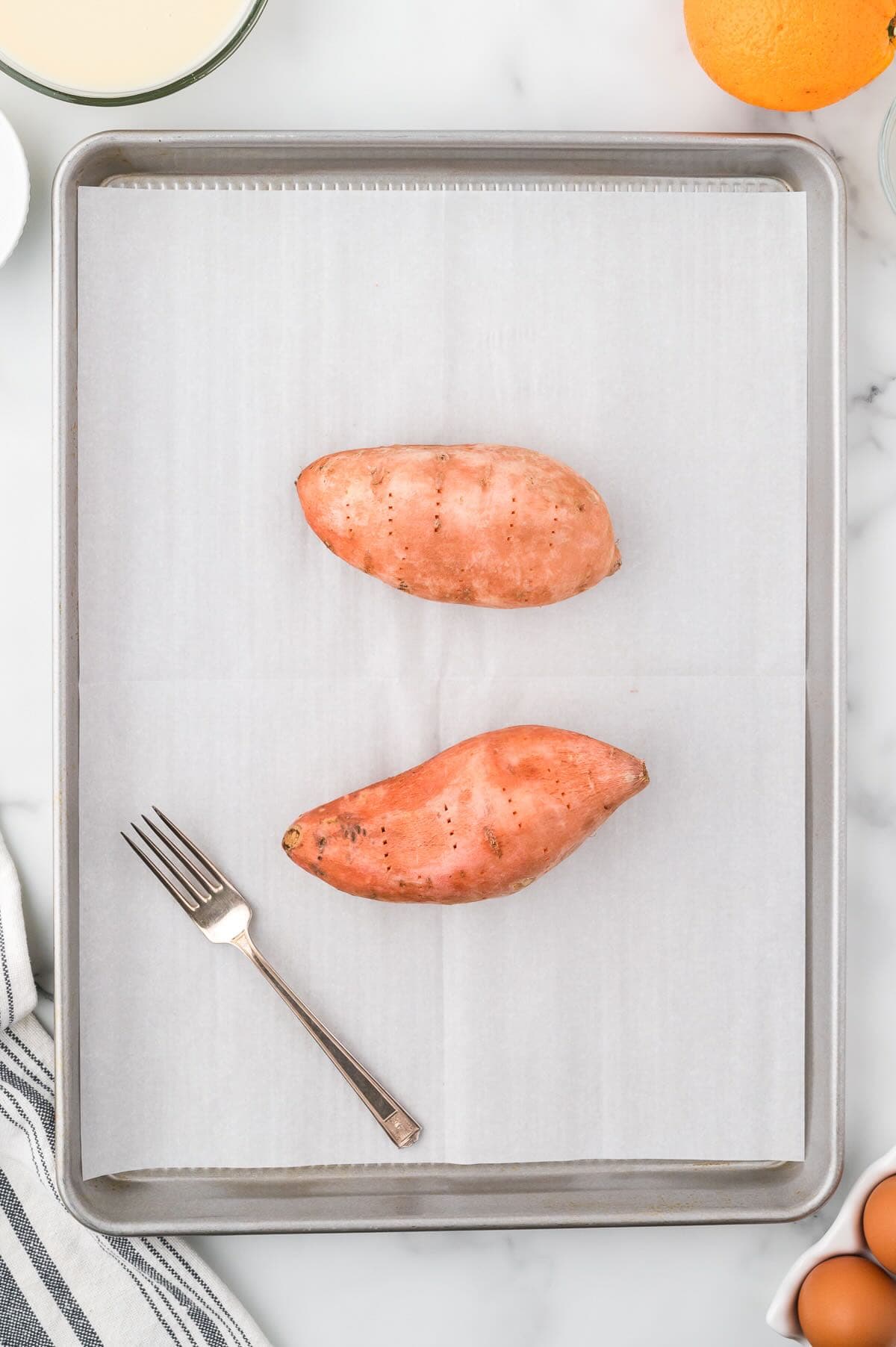 Two sweet potatoes on a baking sheet. 