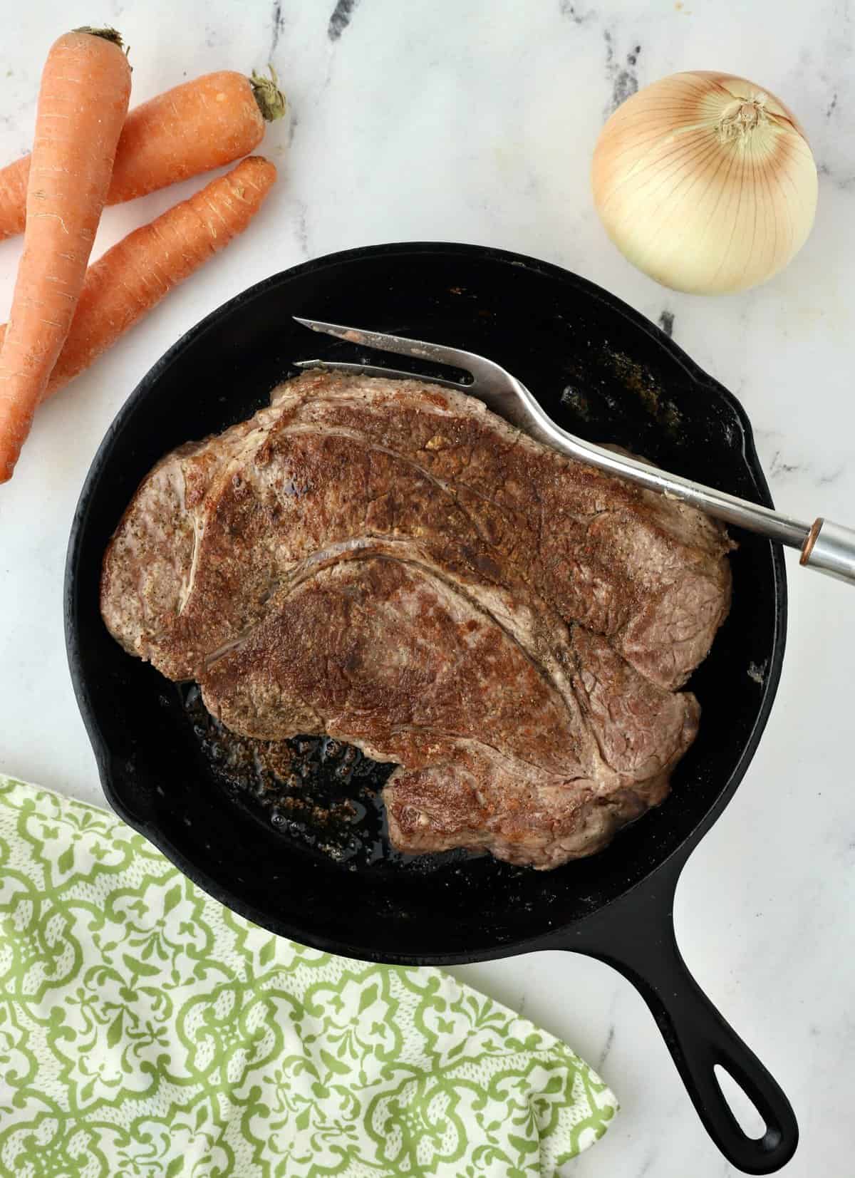 A chuck roast is pan-seared in a cast iron skillet. 