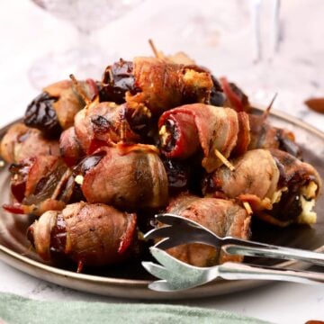 A plate of baked bacon-wrapped stuffed dates with tongs for serving.