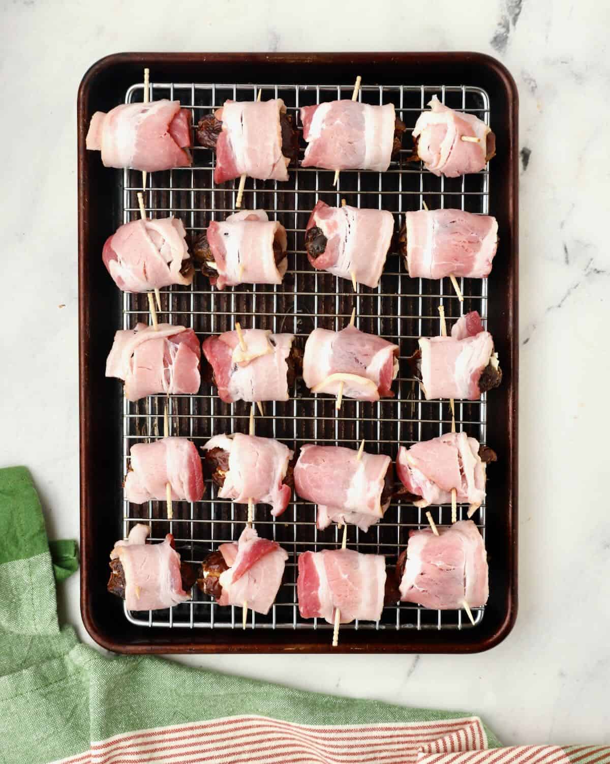 Bacon wrapped dates on a wire rack placed over a baking sheet. 