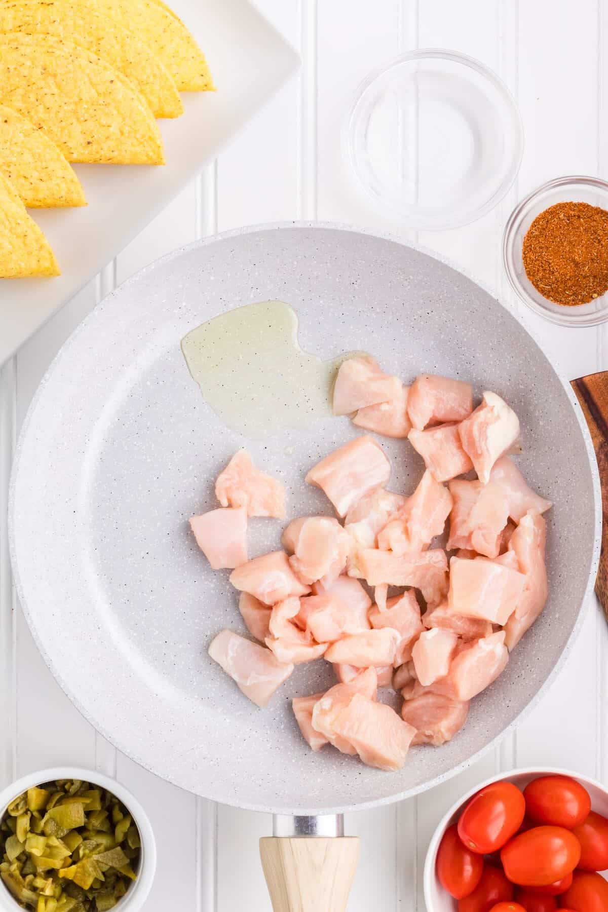 Cubed raw chicken cooking in a white skillet. 