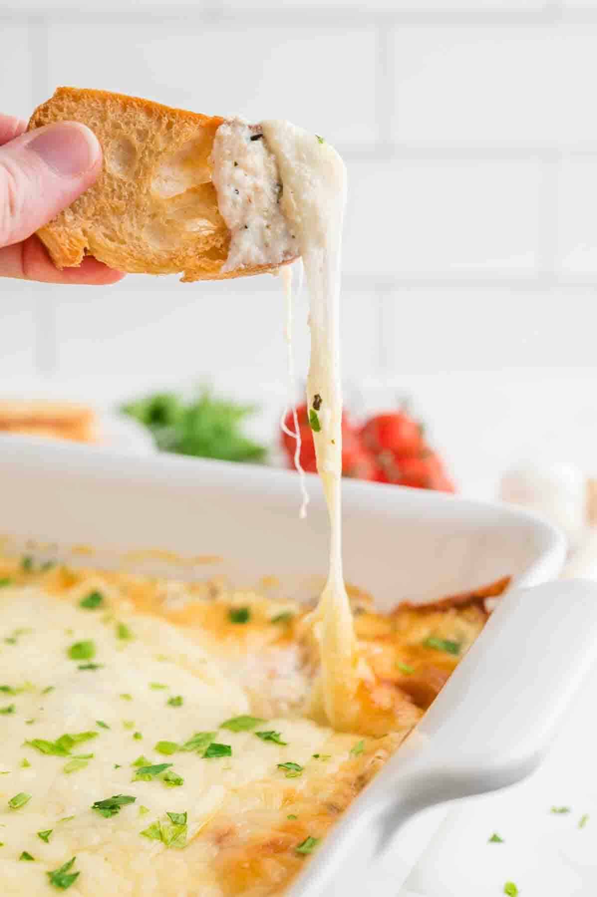 Baked ricotta cheese dip with someone holding a crostini topped with the dip. 