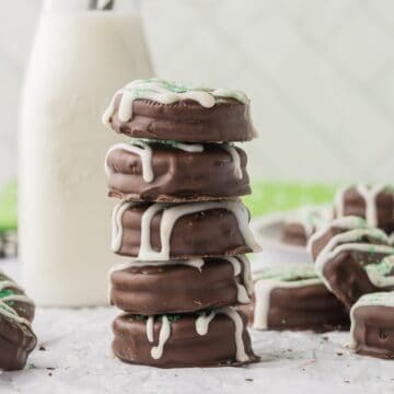 A stack of chocolate covered Oreo cookies next to a bottle of milk.