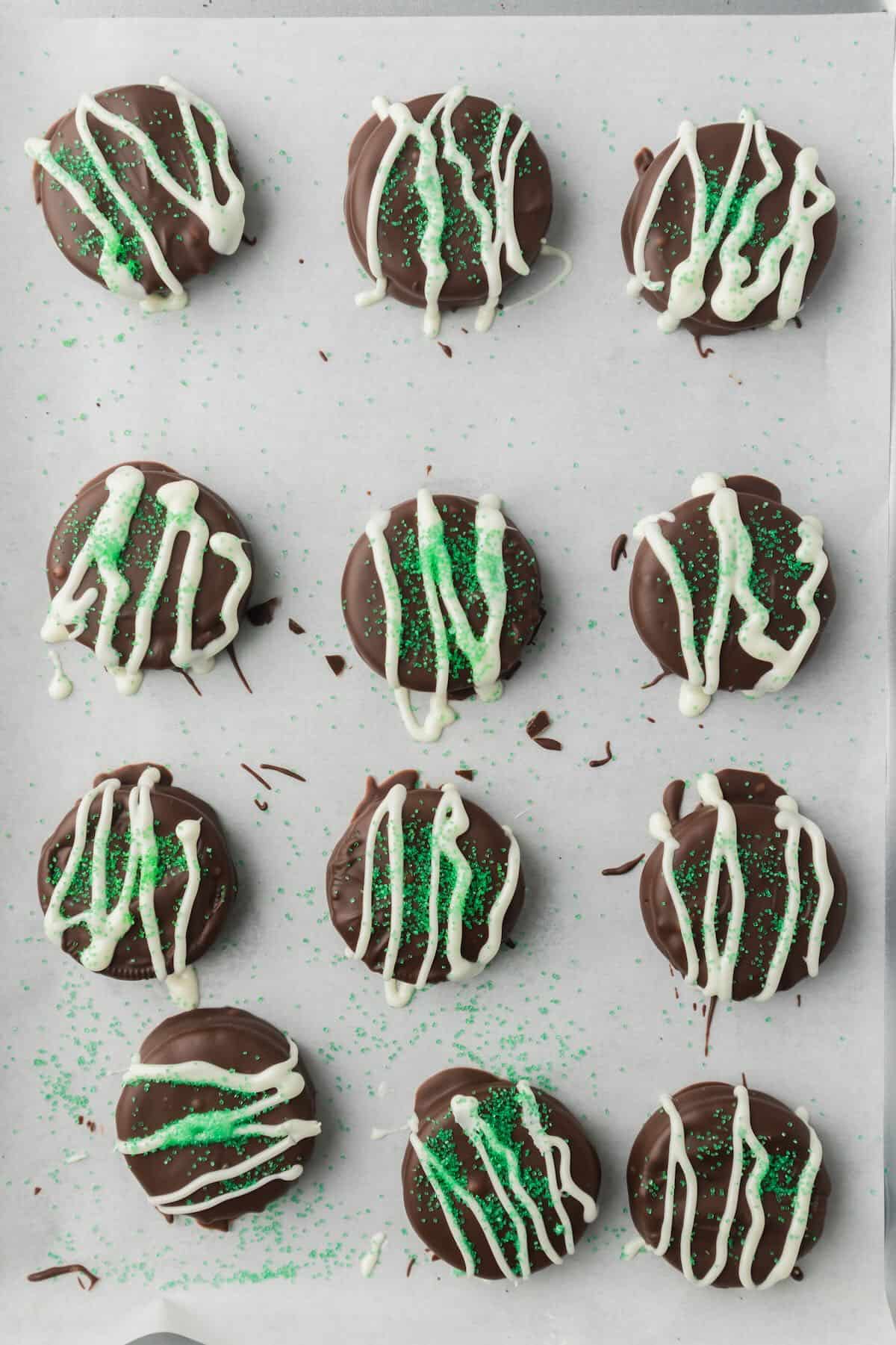 A dozen chocolate-dipped Oreos topped with a drizzle of white chocolate and green sanding sugar. 