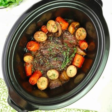 Pot roast in a crock-pot surrounded by potatoes and carrots.