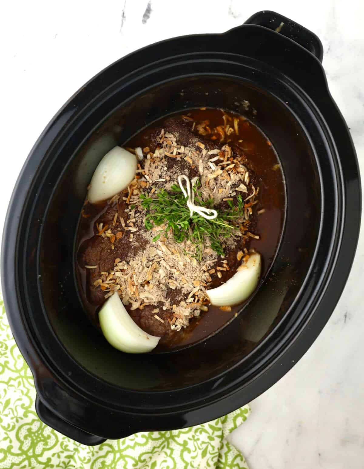 A chuck roast in a crock pot topped with dry soup mix.
