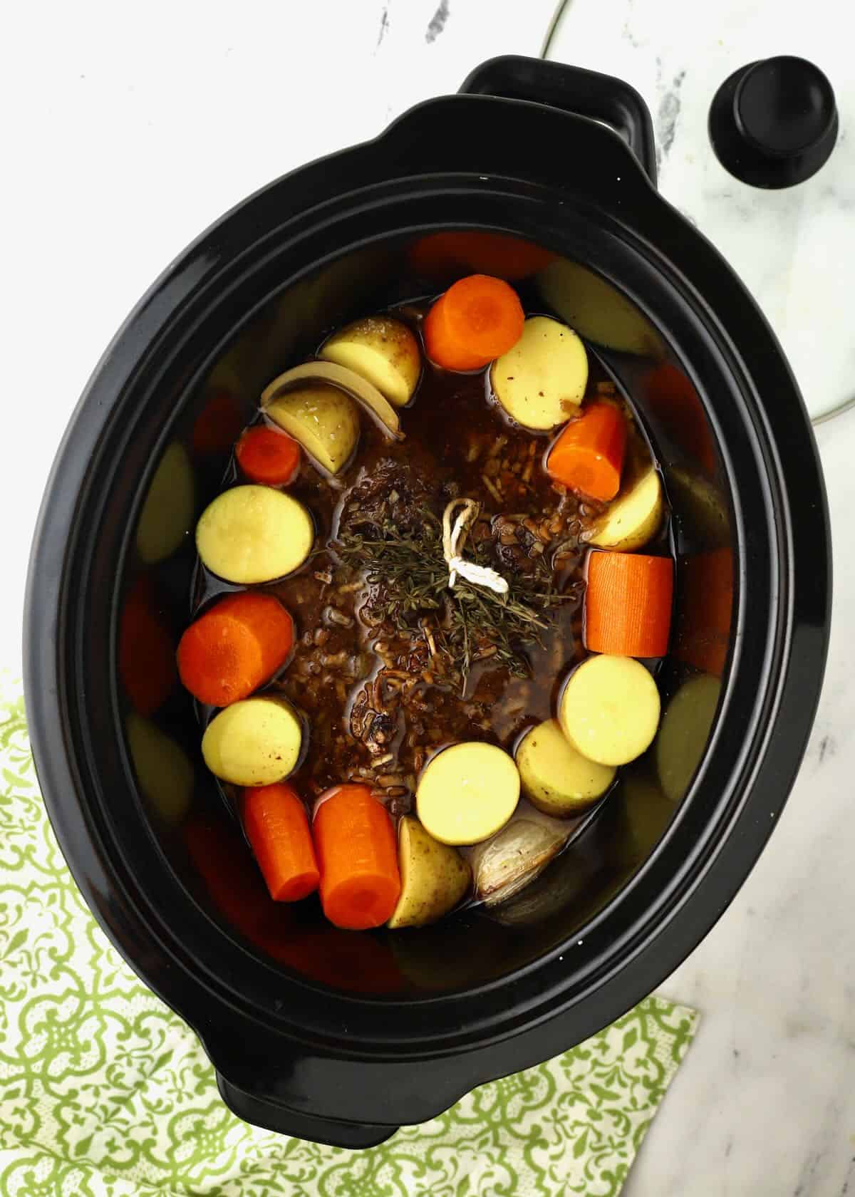 A chuck roast surrounded with potatoes and carrots in a Crock-Pot.