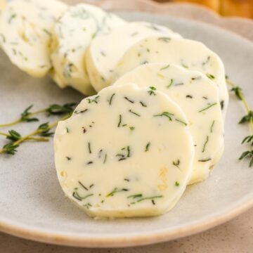 Sliced garlic herb butter on a plate with fresh thyme.