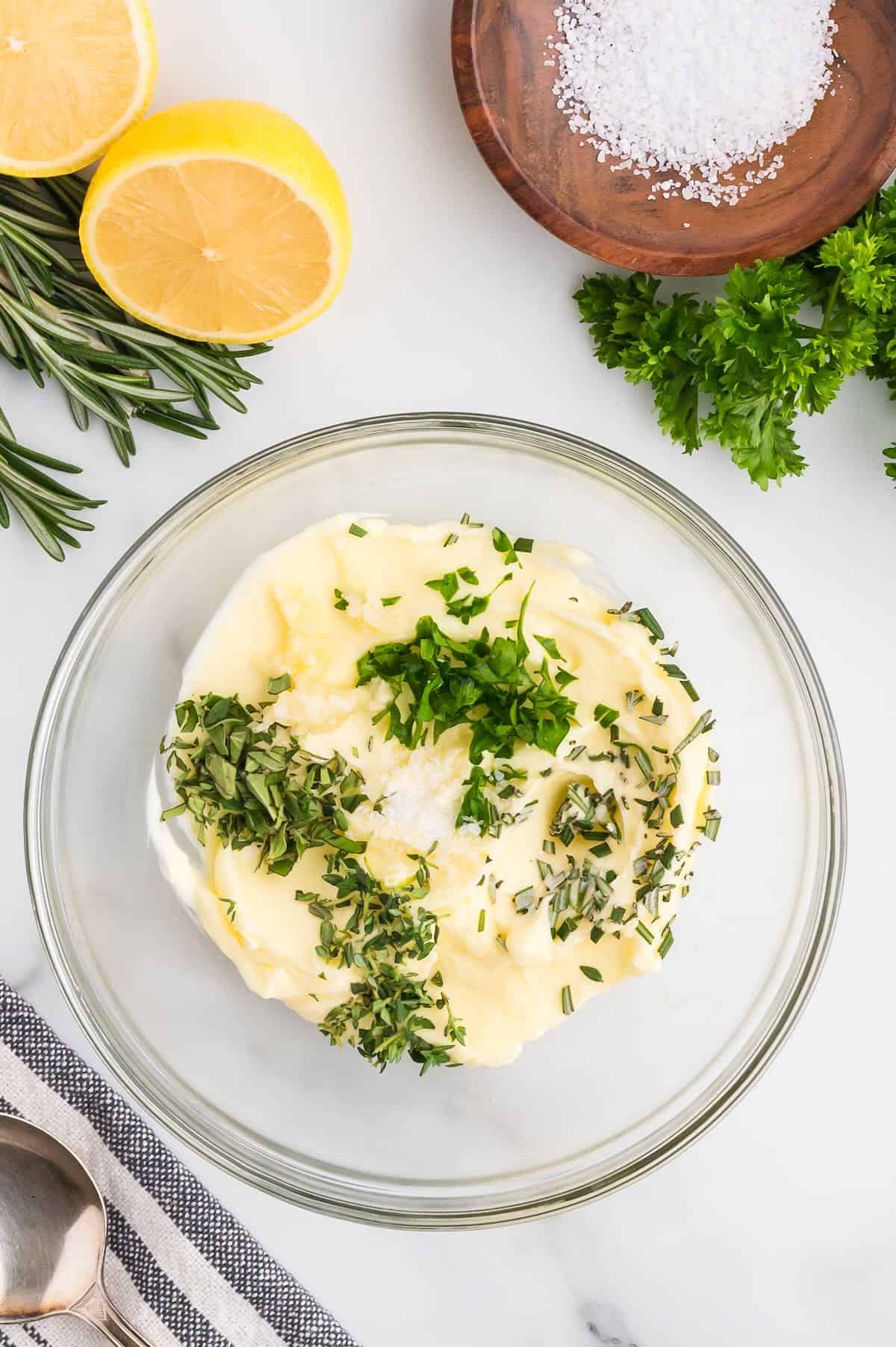 Softened butter in a bowl with chopped fresh herbs on top. 