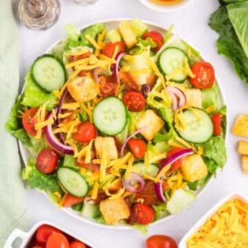 A house salad on a white plate featuring lettuce, tomatoes, cucumbers, cheese and croutons.