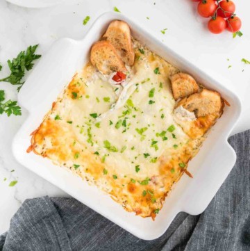 Baked ricotta dip in a white square baking dish topped with fresh chopped parsley.