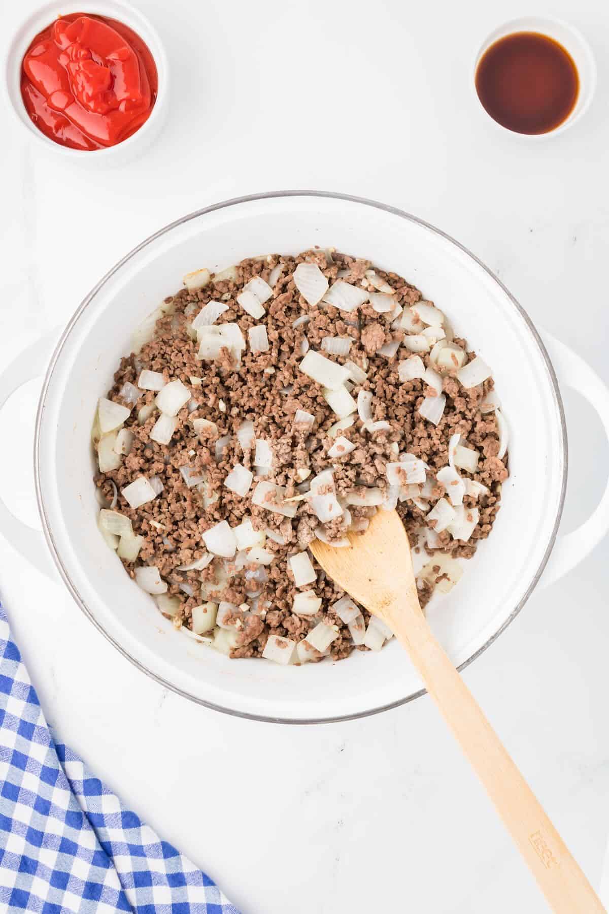 Ground beef and chopped onions cooking in a skillet. 