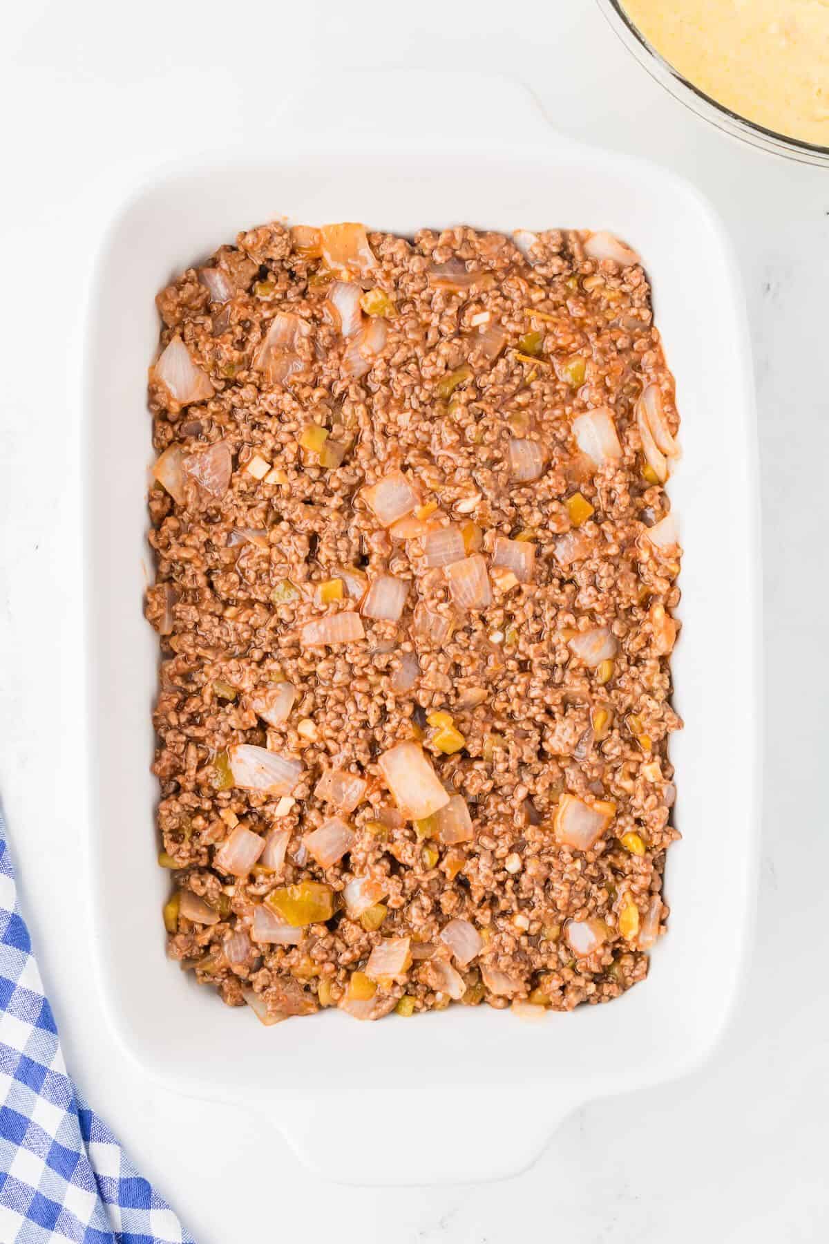 Sloppy joe beef filling spread out in the bottom of a white baking dish. 