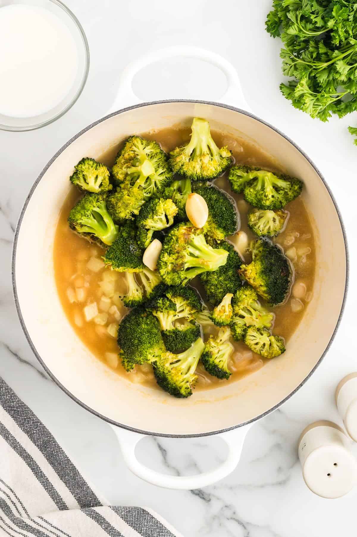 Roasted broccoli is added to a mixture of cannellini beans in a large pot. 