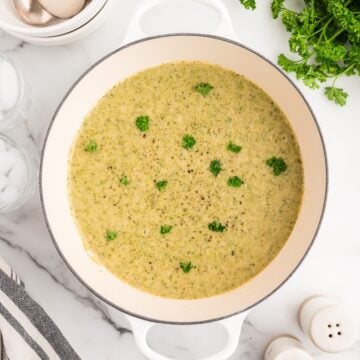 A large white pot of creamy white bean soup garnished with parsley.