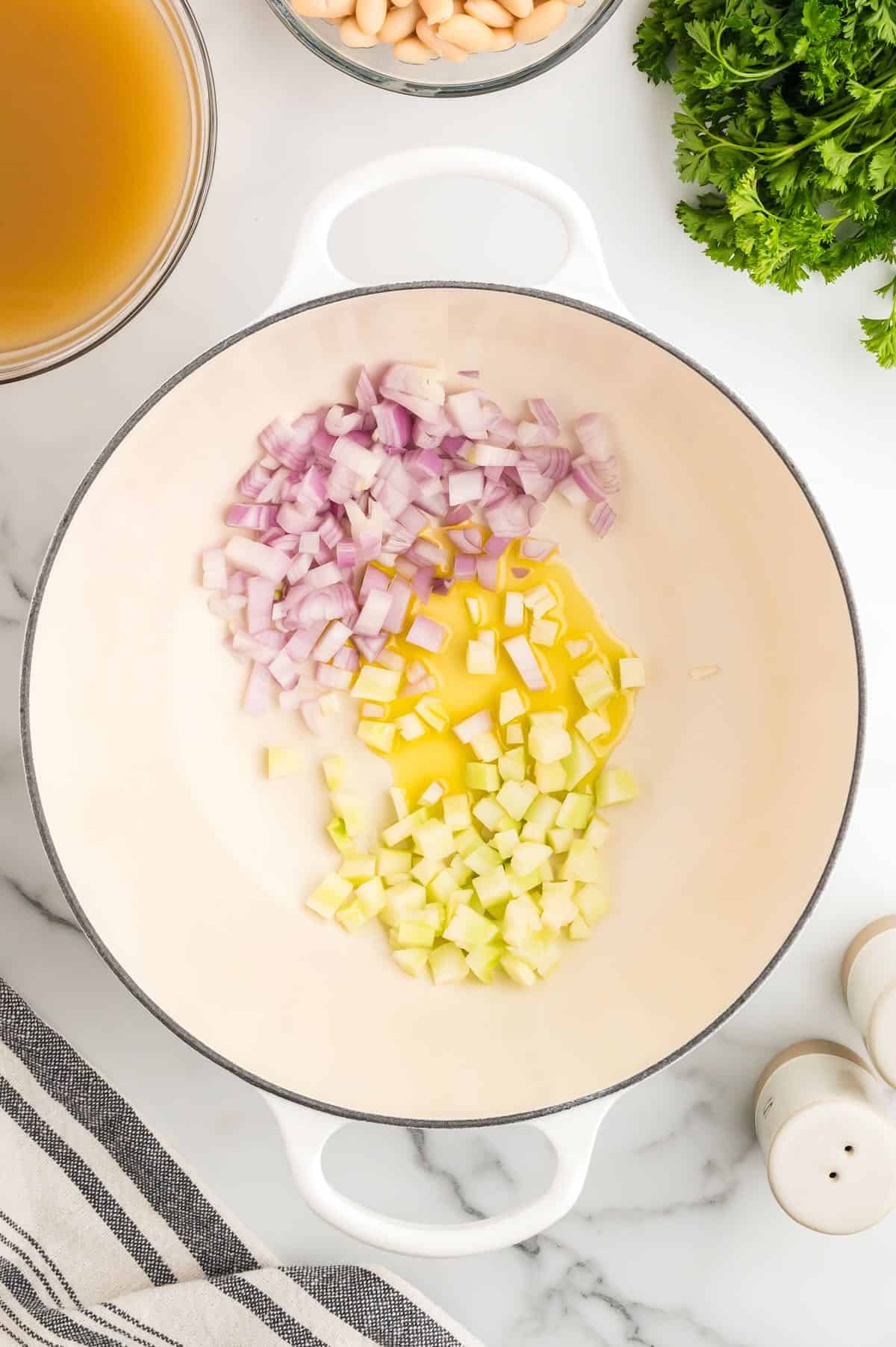 Chopped broccoli stems and shallots cooing in a white pot. 