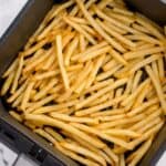 Cooked frozen french fries in an air fryer basket.