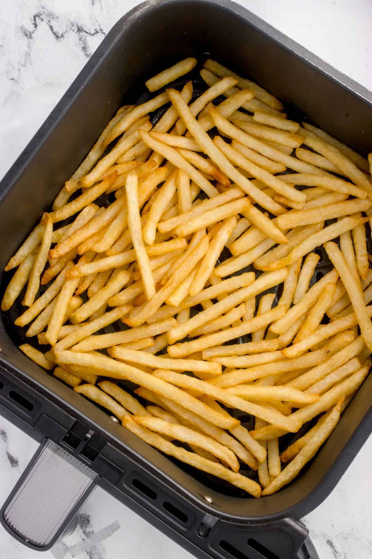 An air fryer basket full of golden brown air-fried french fries. 