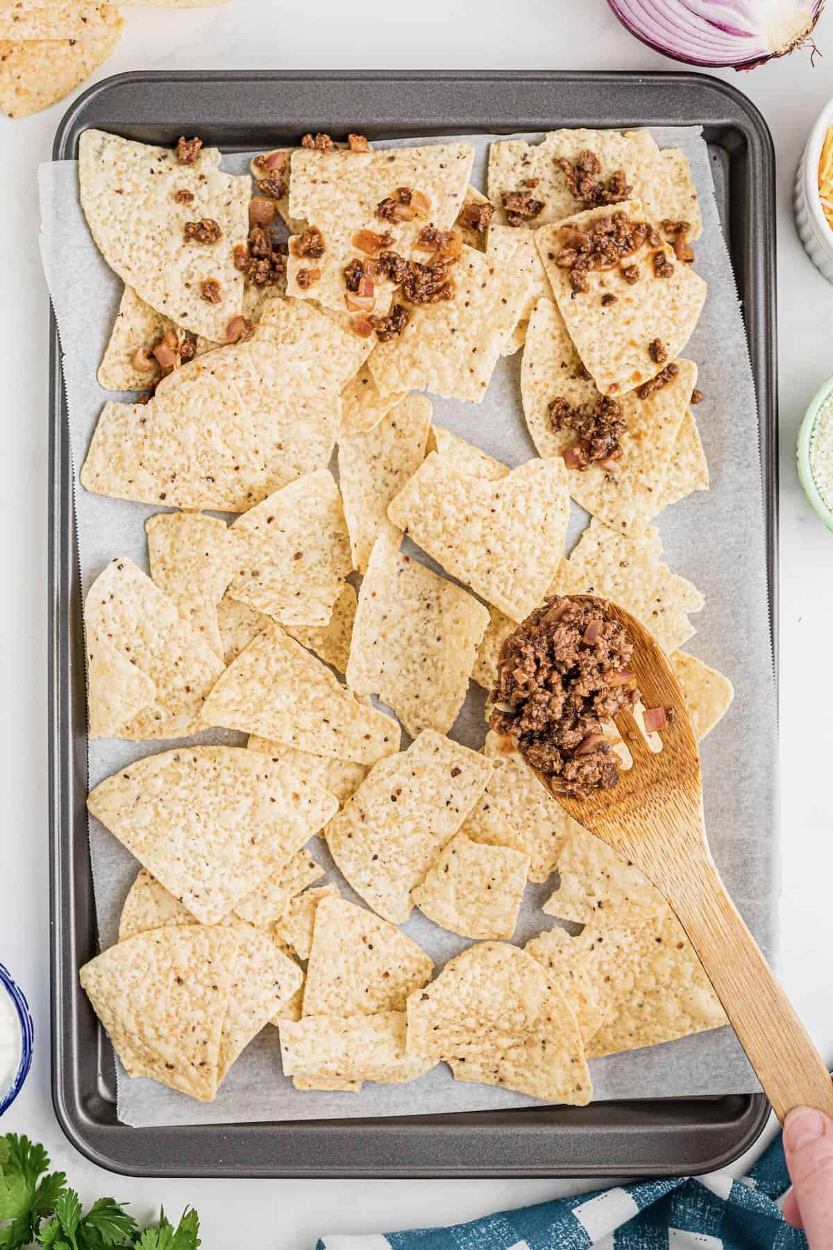 A sheet pan with a layer of tortilla chips topped with beef mixture. 