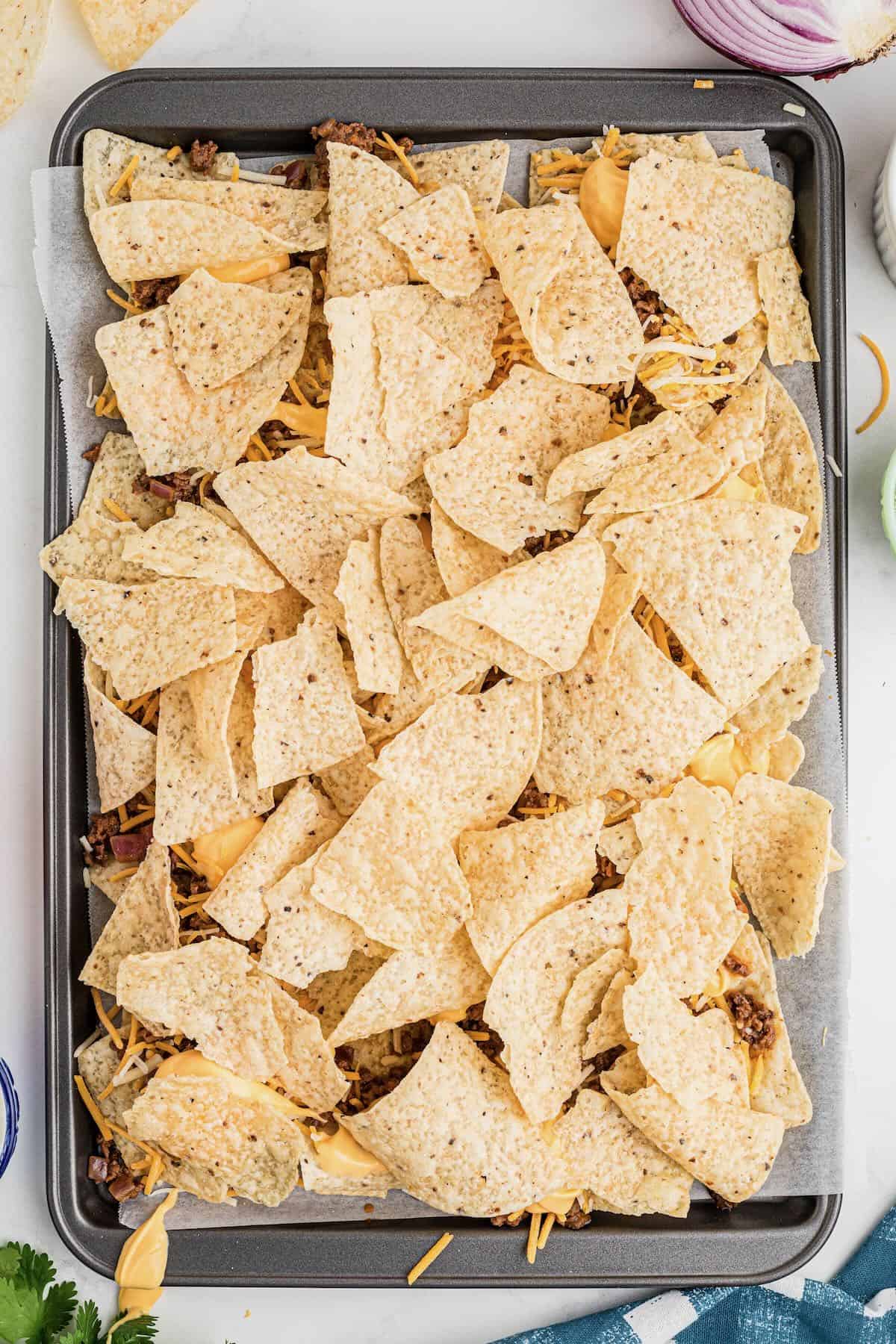 A sheet pan with two layers of tortilla chips, cooked ground beef and cheese. 