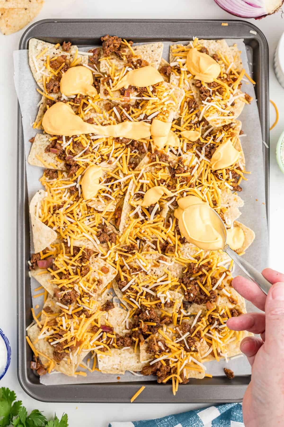 A sheet pan with tortilla chips, cooked ground beef, and cheese. 