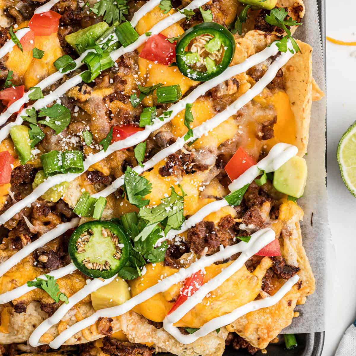 A sheet pan full of beef nachos topped with sour cream.