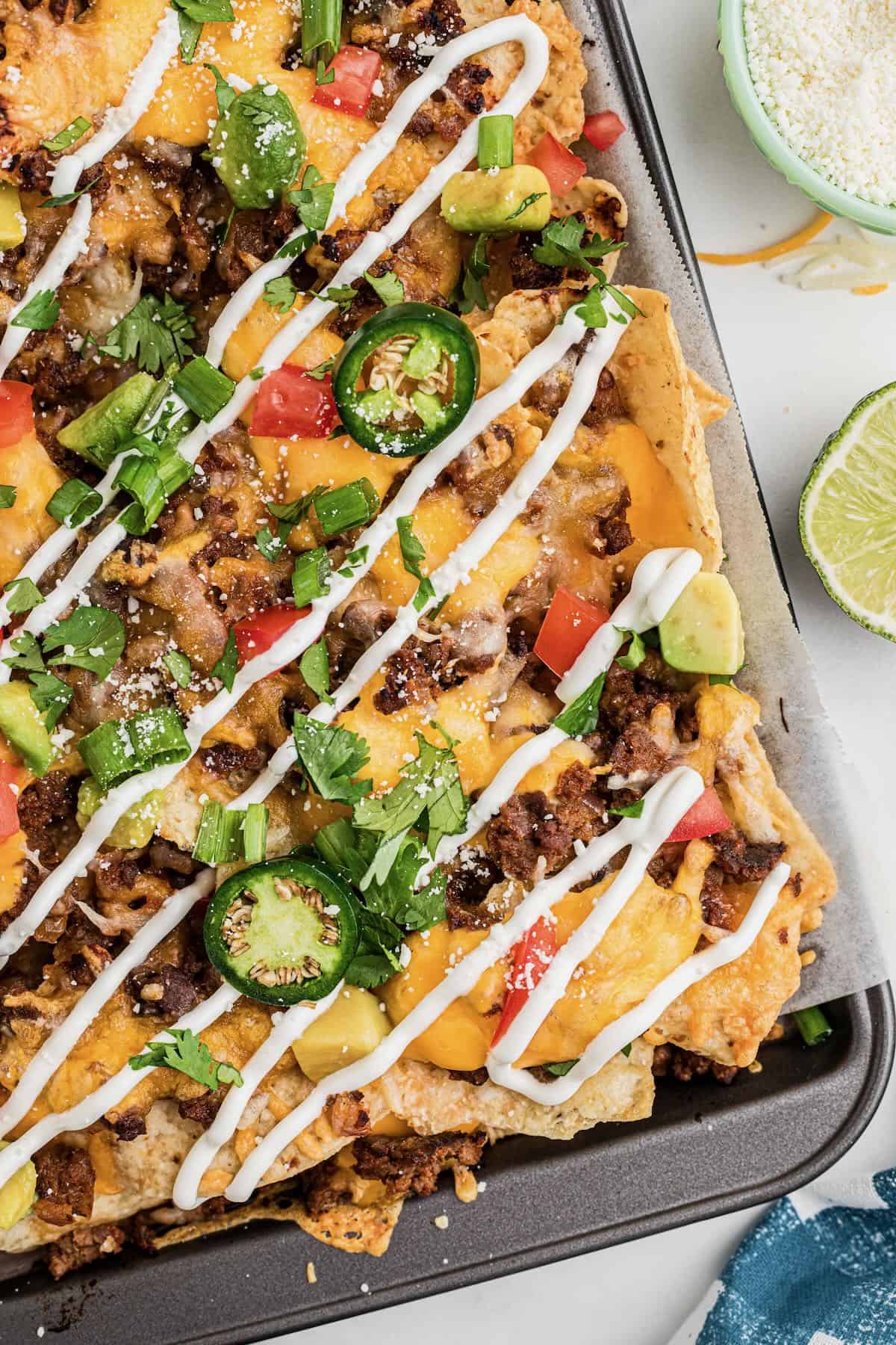 A sheet pan full of loaded beef nachos with toppings. 