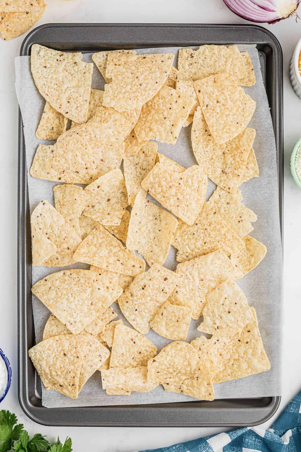 A rimmed baking sheet covered with a layer of tortilla chips. 