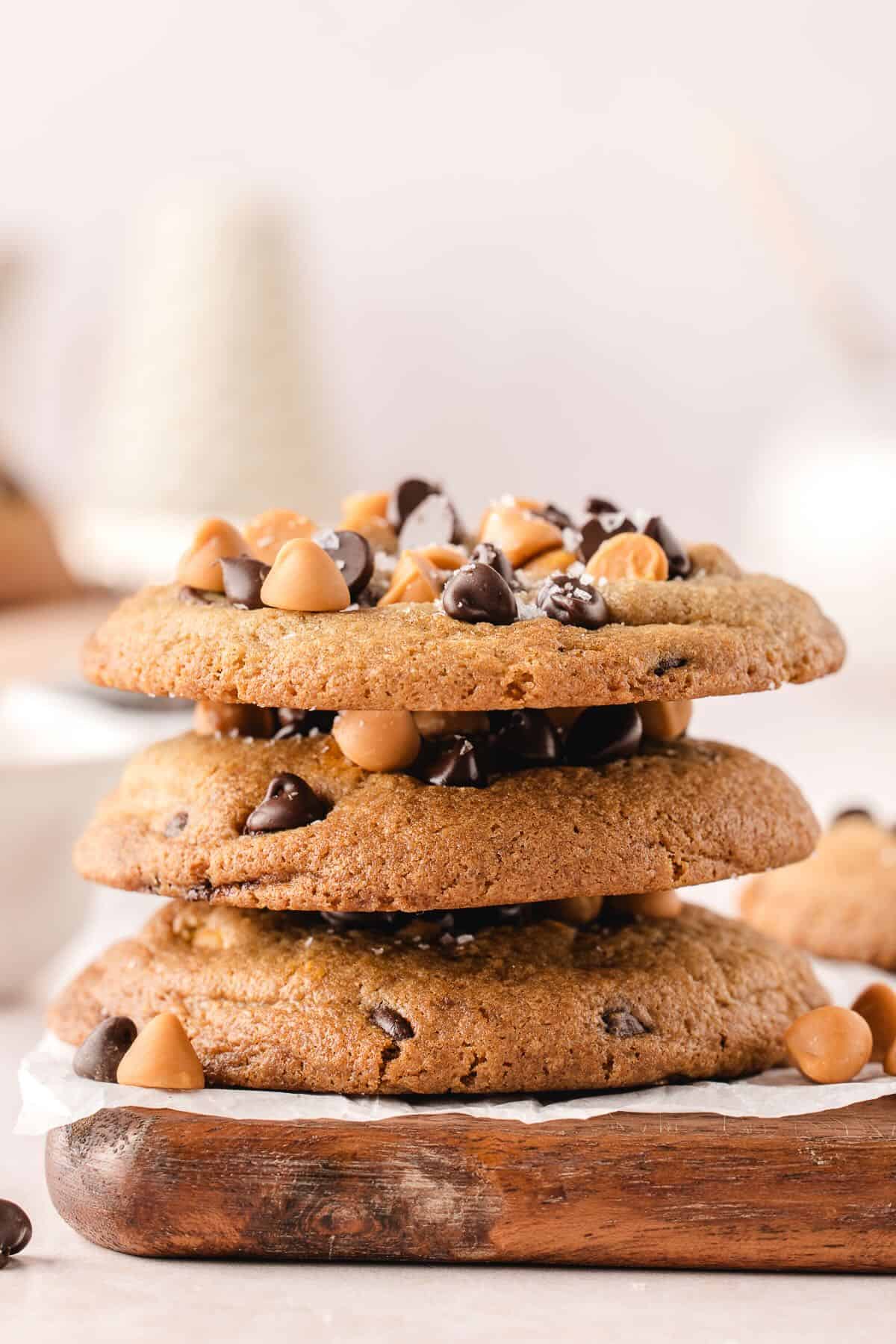 Three butterscotch chocolate chip cookies stacked on a cutting board. 