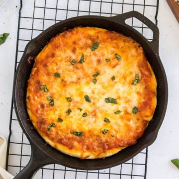 A cast iron skillet pizza just out of the oven with a golden brown crust and melted cheese.