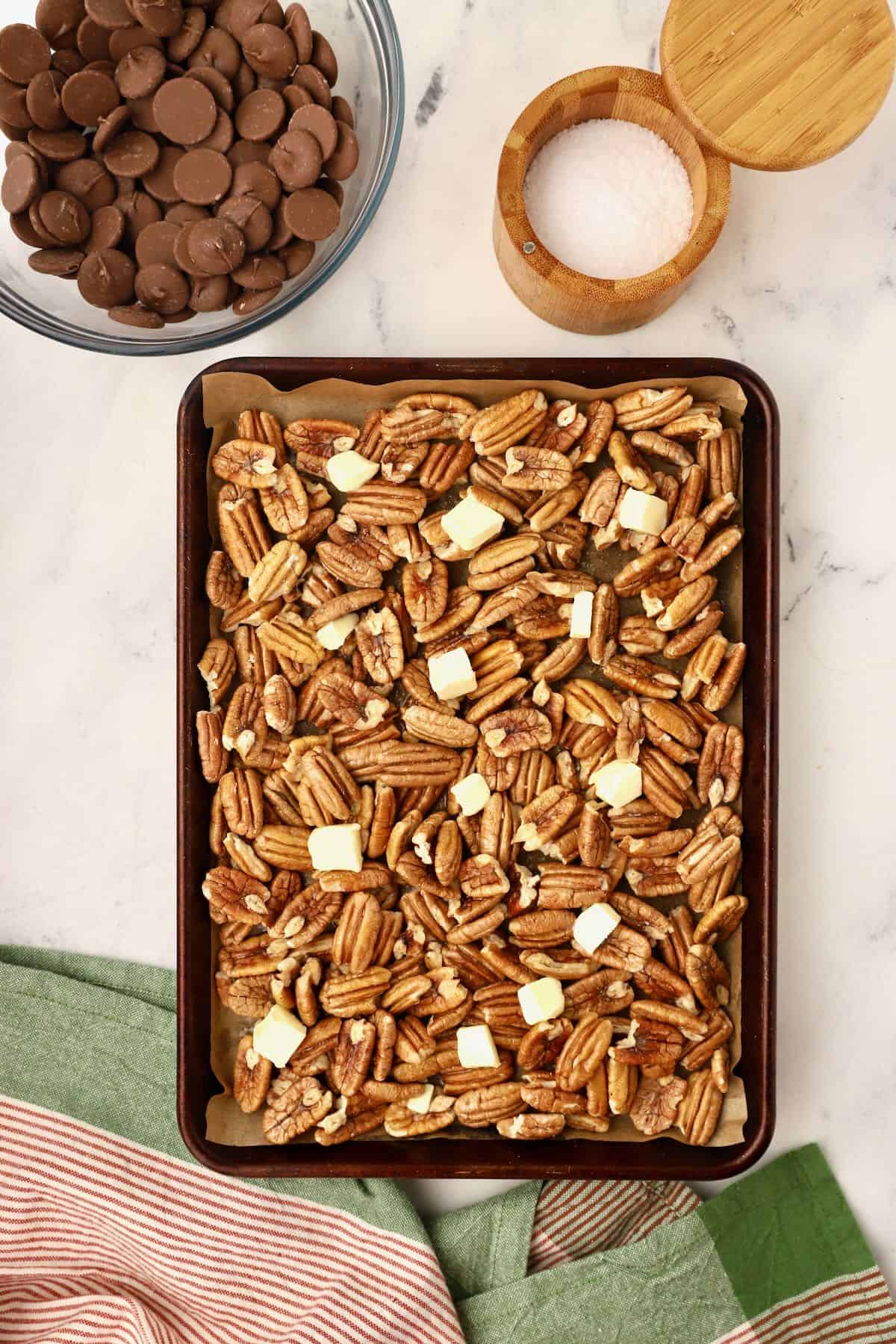 A sheet pan full of pecans with small cubes of butter dotting the top. 