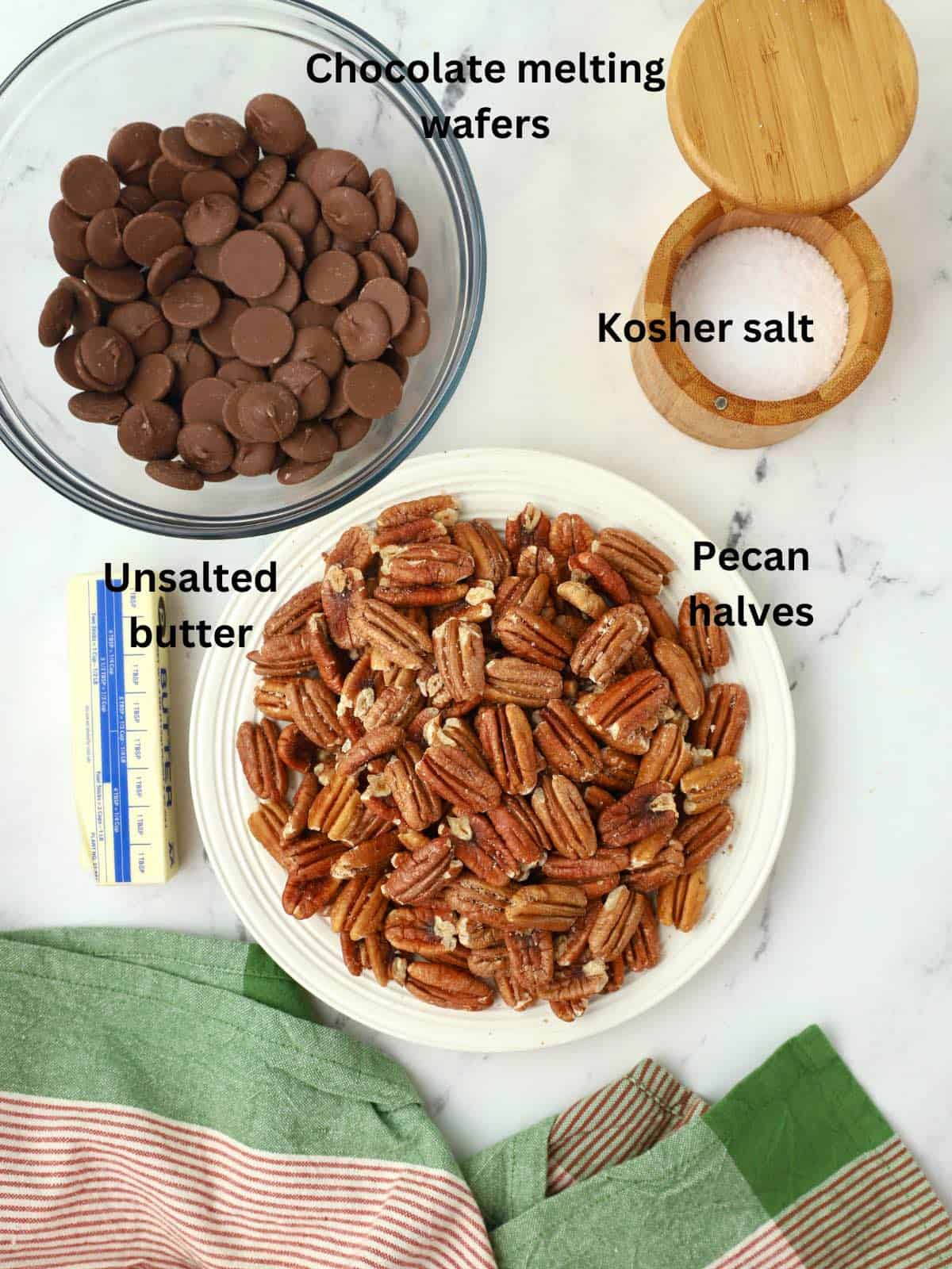 A plate of pecan halves, a bowl of chocolate melting wafers, salt, and a stick of butter. 