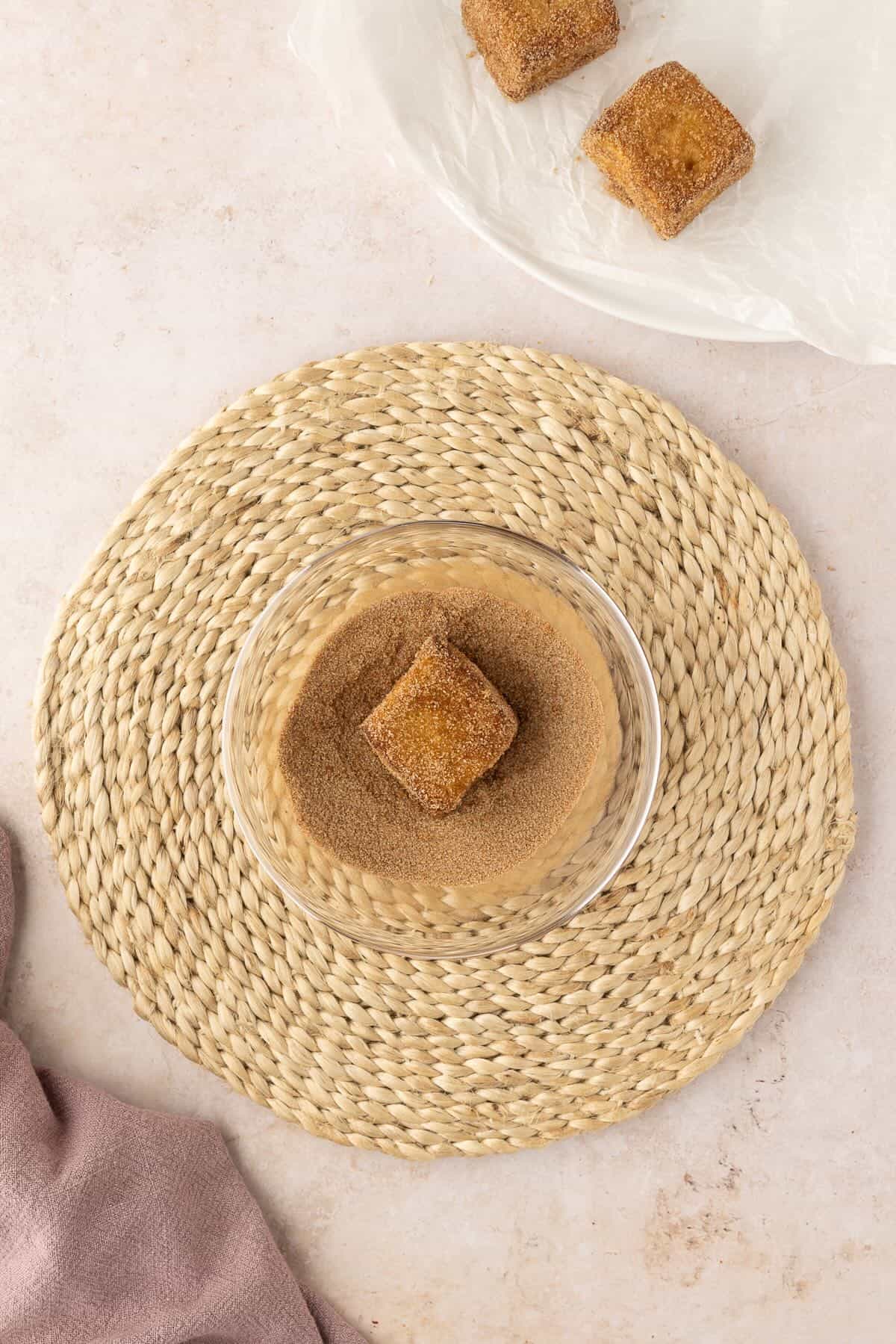 A French Toast Bite is coated in cinnamon sugar in a small bowl. 