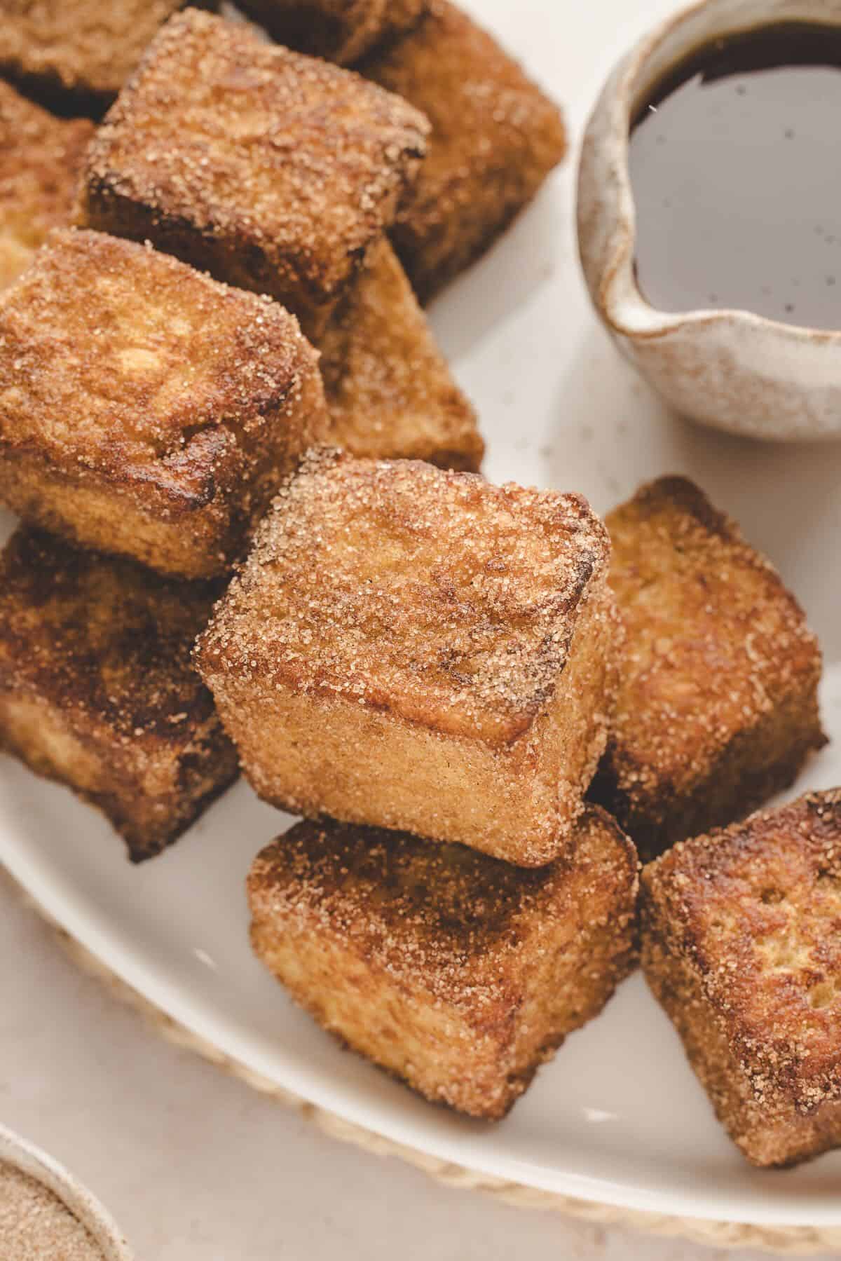 Pan fried French Toast Bites on a plate with a pitcher of syrup. 