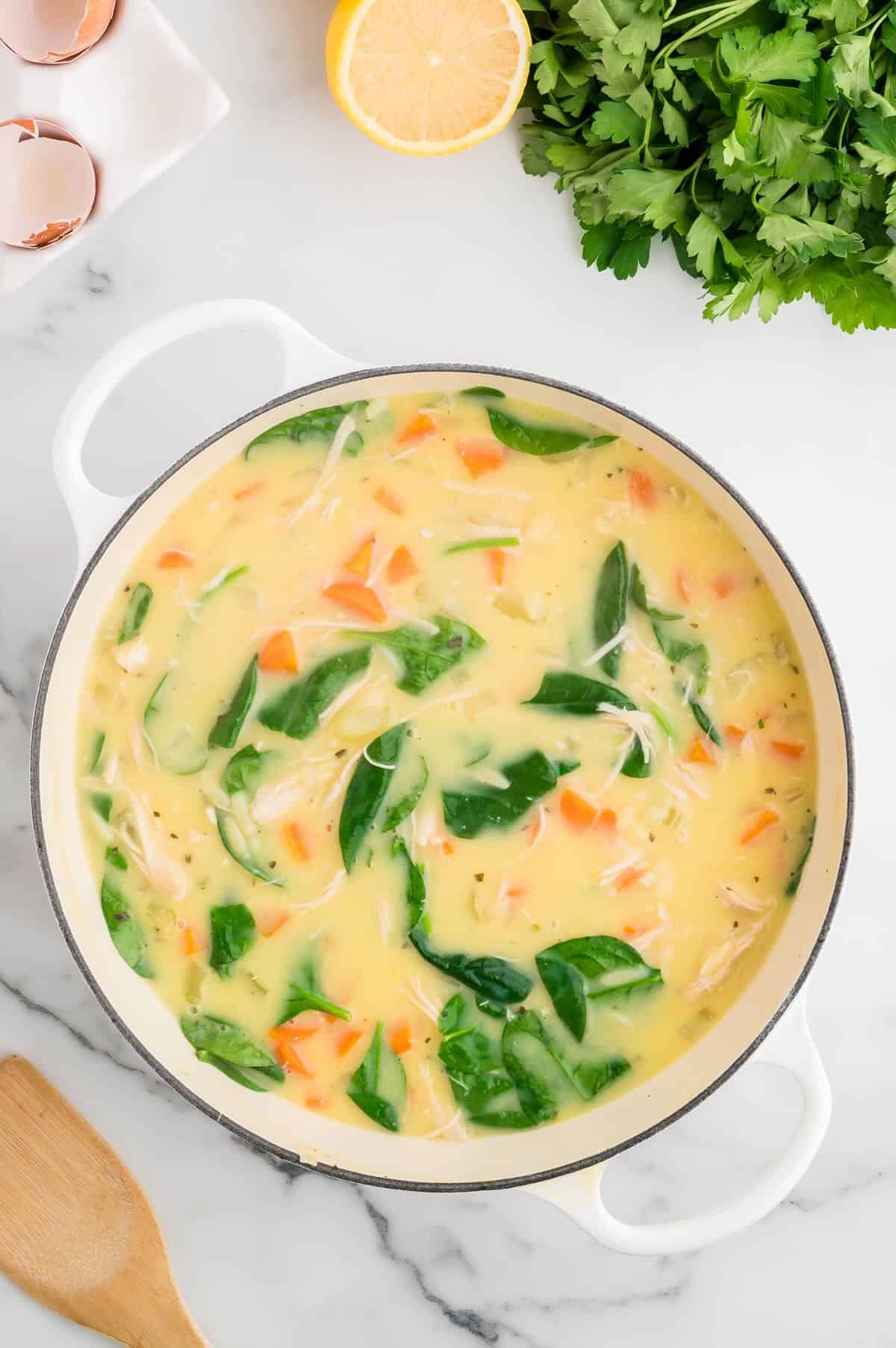 Fresh spinach is added to a soup pot with Greek lemon soup. 