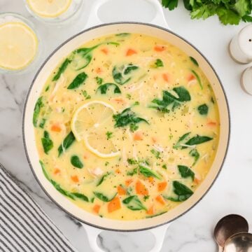 Greek Chicken Soup with Lemon and Orzo in a white Dutch oven with wilted spinach.