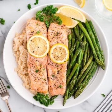 Two lemon pepper salmon fillets topped with lemon slices with brown rice and asparagus.