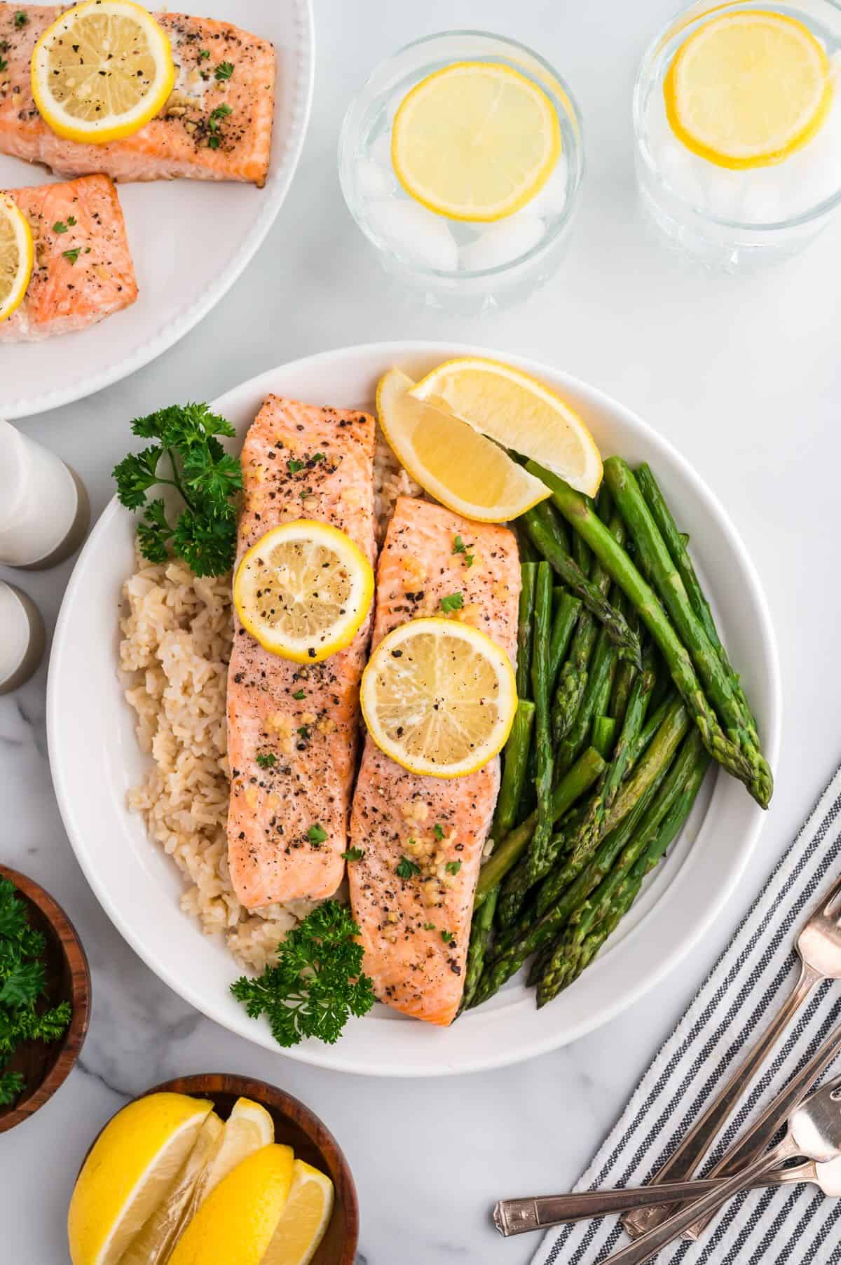 A white plate with cooked brown rice, asparagus, and two baked salmon fillets. 
