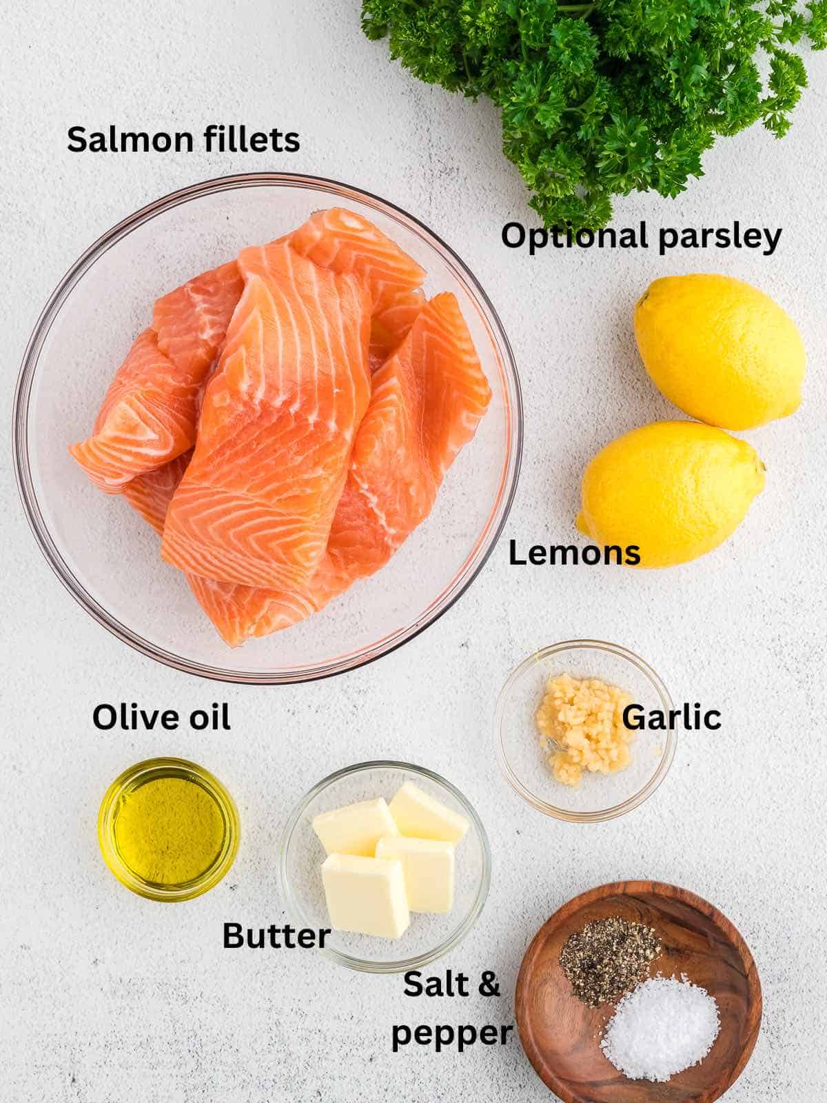 Ingredients on a counter including salmon fillets, lemons, parsley and pats of butter. 