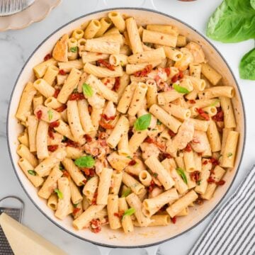 Marry Me Chicken Pasta in a white skillet topped with fresh basil leaves.