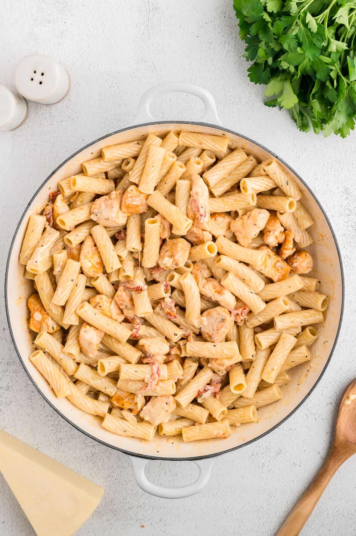 Cooked pasta, chicken, and a creamy sauce in a white skillet. 