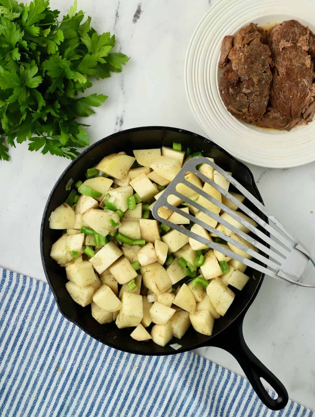 Cubed potatoes and bell pepper cooking in a cast iron skillet. 