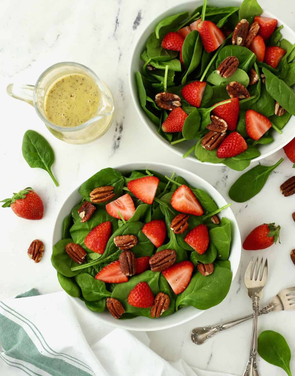 Two bowls of spinach strawberry salad with poppy seed dressing ready to serve.