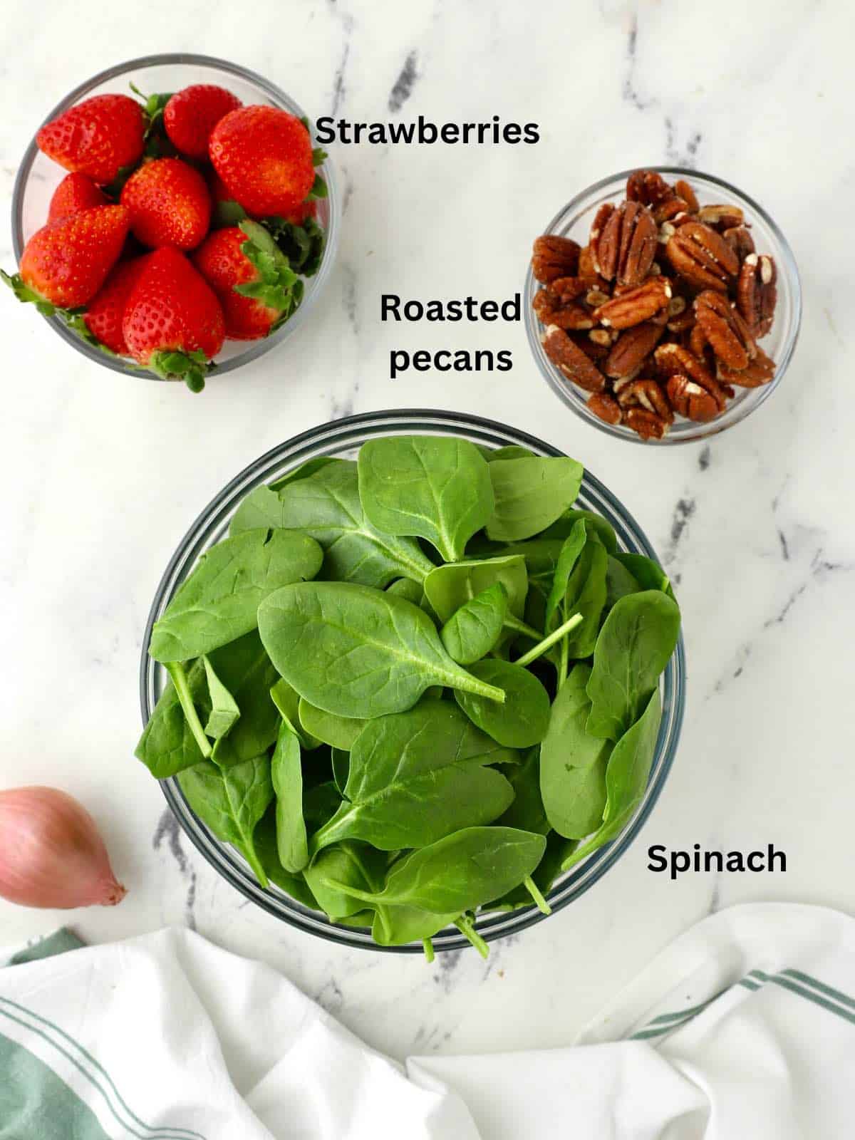 A large bowl of fresh spinach leaves, ripe strawberries, and roasted pecans. 