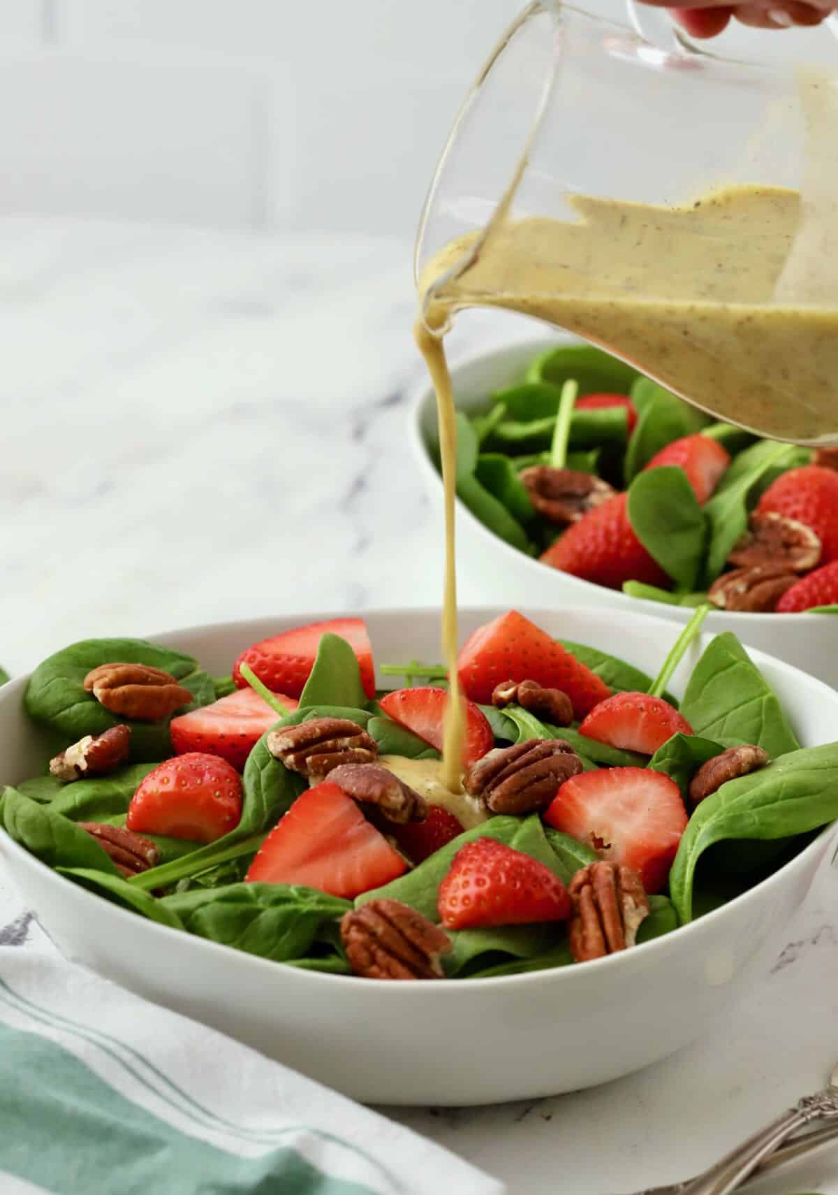 Pouring poppyseed dressing from a pitcher onto spinach salad. 