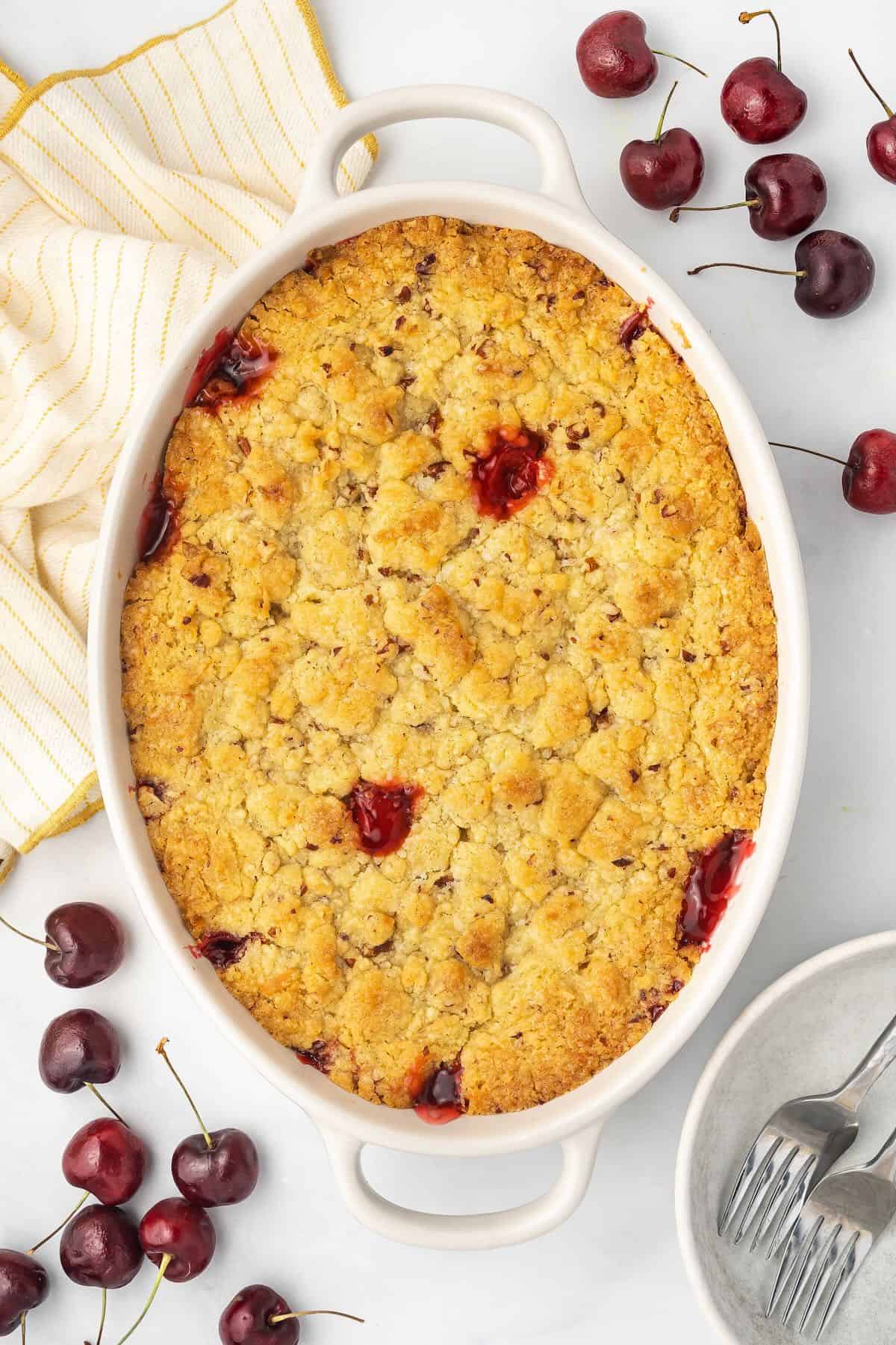Baked cherry cobbler with a golden brown topping in a white baking dish. 